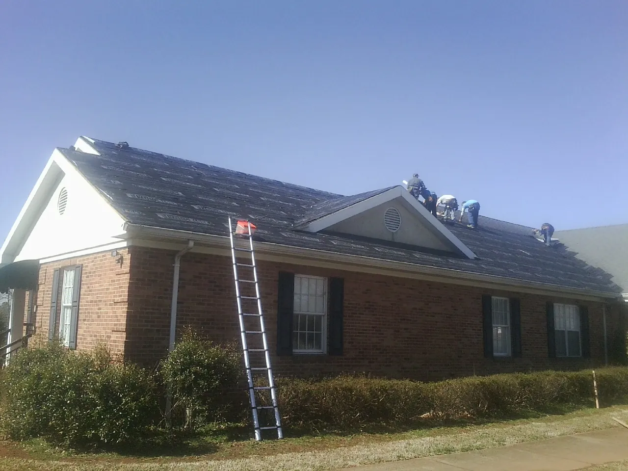 Crew tearing shingles off a brick ranch roof with a ladder set — Metal Roof Repair work by our crew in Hayfork