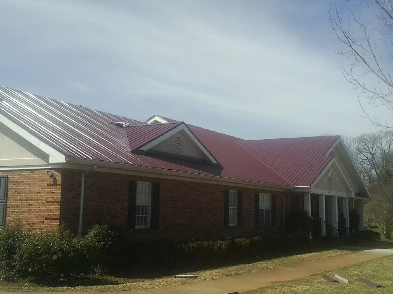 Red metal roof with gabled entries on a long brick building, from a Hail Damage Roof Repair job in Hayfork