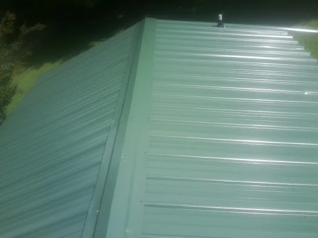 New green metal panels meeting at the ridge of a roof — Flat Roof Repair work by our crew in Hayfork