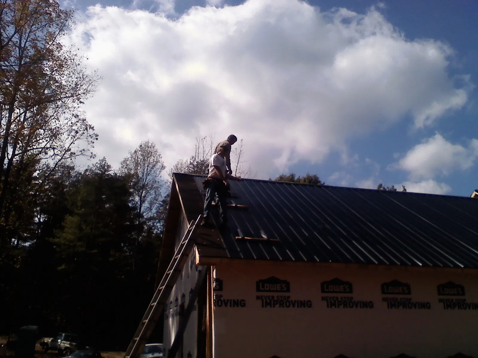 Roofer fastening dark metal panels high against a cloudy sky, from a Roof Inspection job in Hayfork